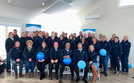 group photo of employees sitting together and smiling for the camera, some holding blue balloons