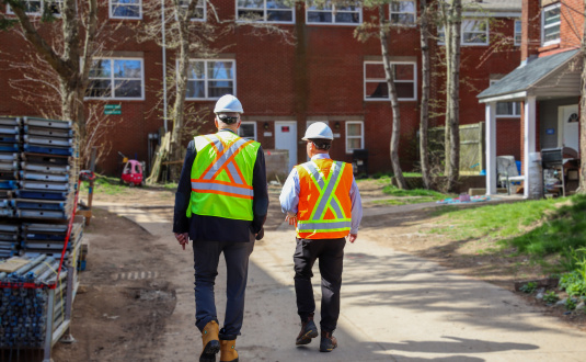 Two men in construction gear walking towards a building under construction