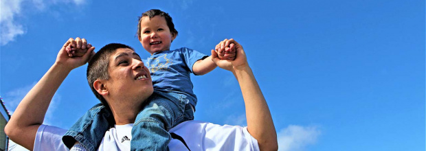 toddler sits on his fathers shoulders backdropped by a clear sky